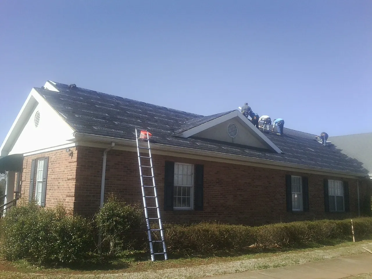 Crew tearing shingles off a brick ranch roof with a ladder set — Metal Roof Repair work by our crew in Waynesboro