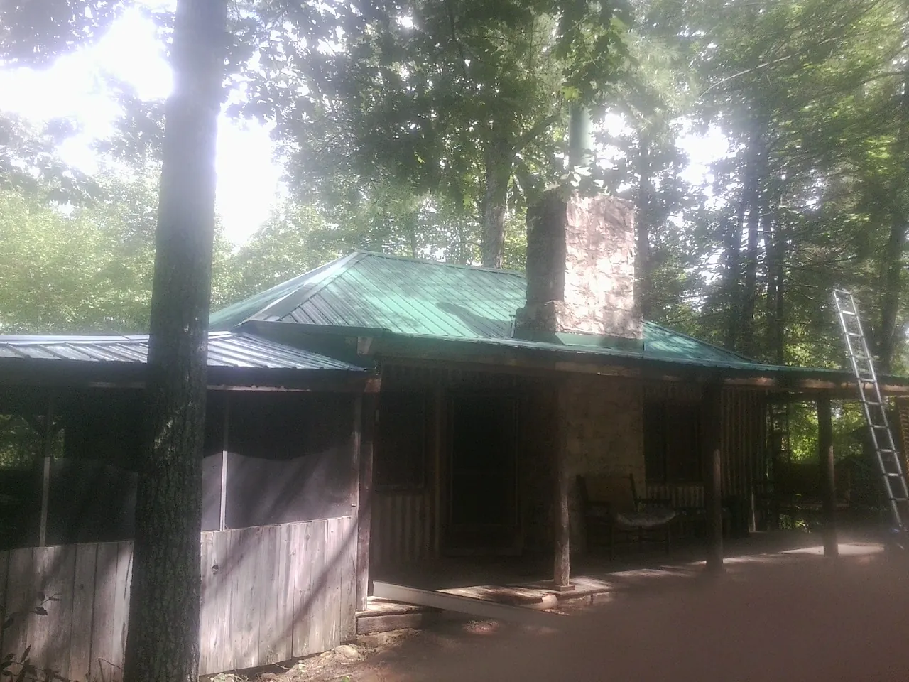 Green metal roof and stone chimney above a log cabin porch in Waynesboro